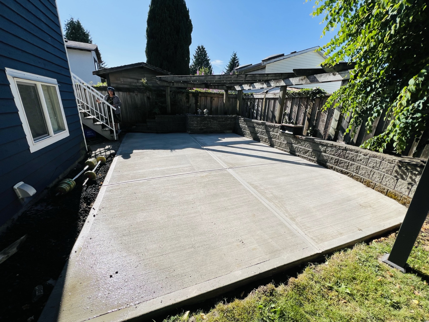 Finished concrete patio alongside a house and a timber retaining wall