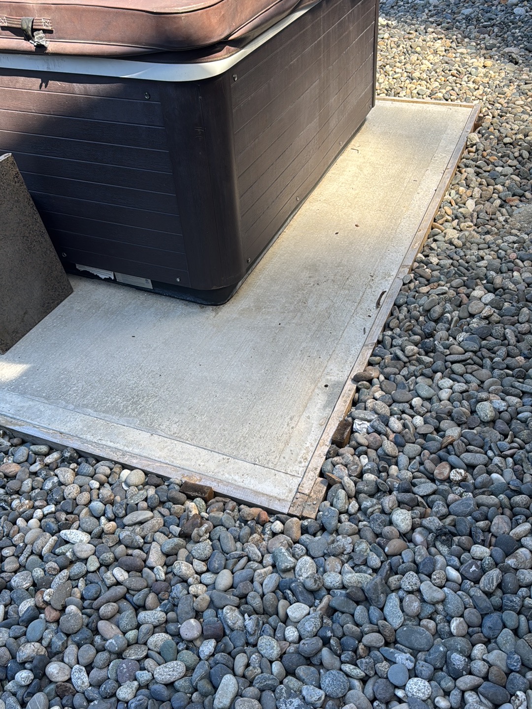 Hot tub sitting on a finished concrete pad with river rock around it